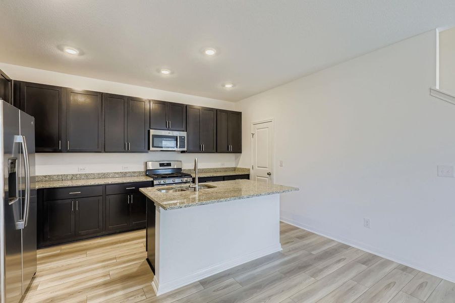 Kitchen with stainless steel appliances, light stone counters, a center island with sink, light wood-style flooring, and recessed lighting Kitchen with stainless steel appliances, light stone counters, a center island with sink, light wood-style flooring, and recessed lighting
