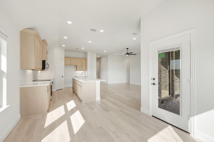Open-concept kitchen with light wood cabinets, center island, and light hardwood floors leading to living area
