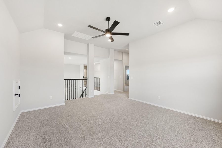 Open upstairs loft area with carpet, black ceiling fan, and iron stair railing visible in background Open upstairs loft area with carpet, black ceiling fan, and iron stair railing visible in background