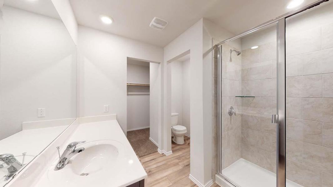 Contemporary bathroom featuring a spacious vanity with an integrated sink, a large wall-mounted mirror, a glass-enclosed shower with tiled walls and a built-in shelf, recessed lighting, and wood-finish flooring