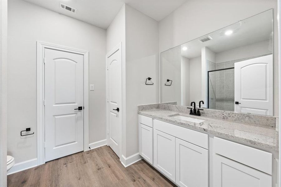 Bathroom with vanity, toilet, LVP flooring, and walk in shower.