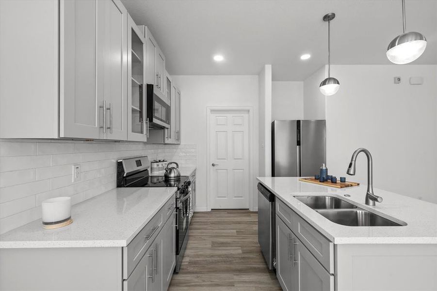 Kitchen featuring wood finished floors, gray cabinets, a sink, stainless steel appliances, and backsplash