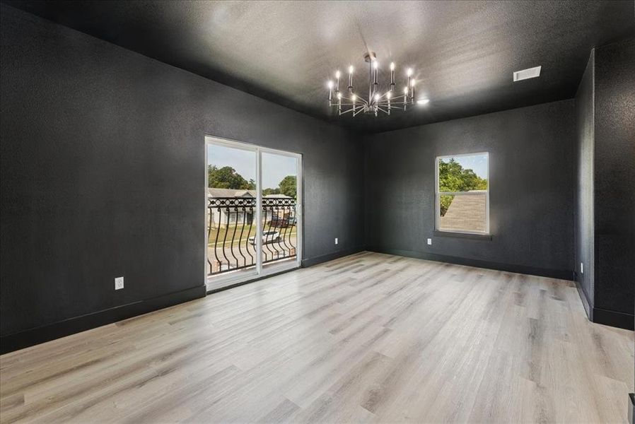 Empty room featuring a chandelier, light wood-type flooring, a textured wall, and a textured ceiling