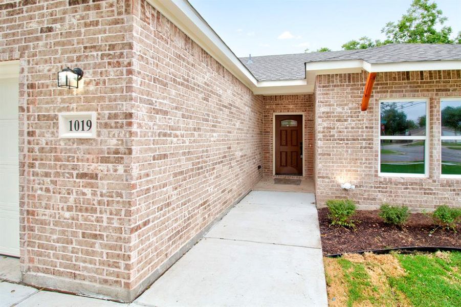 Entrance to property featuring brick siding, a garage, and roof with shingles