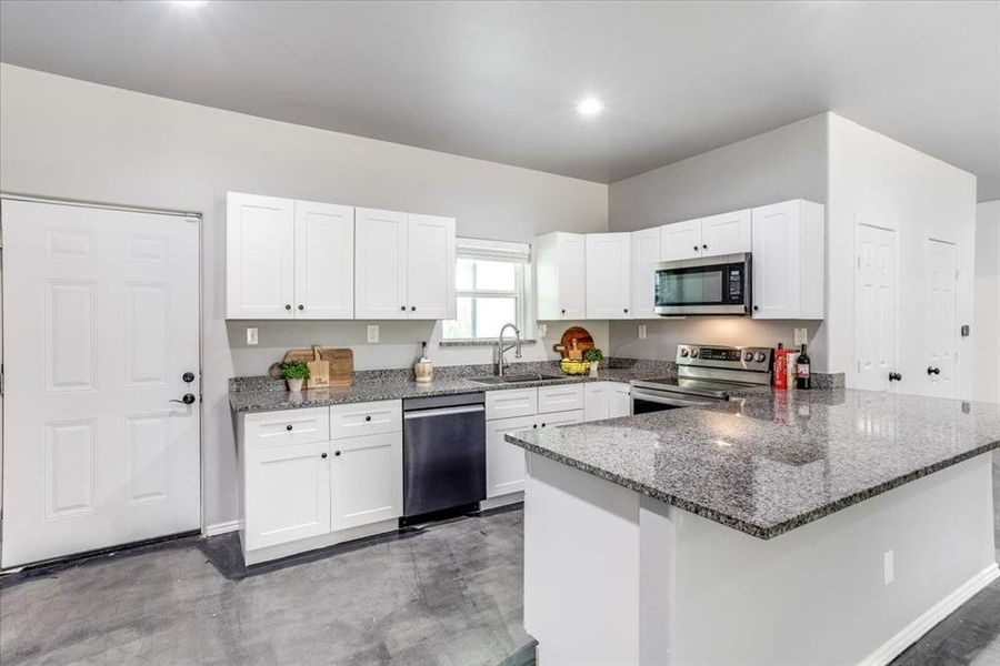 Modern kitchen featuring white shaker cabinetry, stainless steel appliances, granite countertops, and a central island