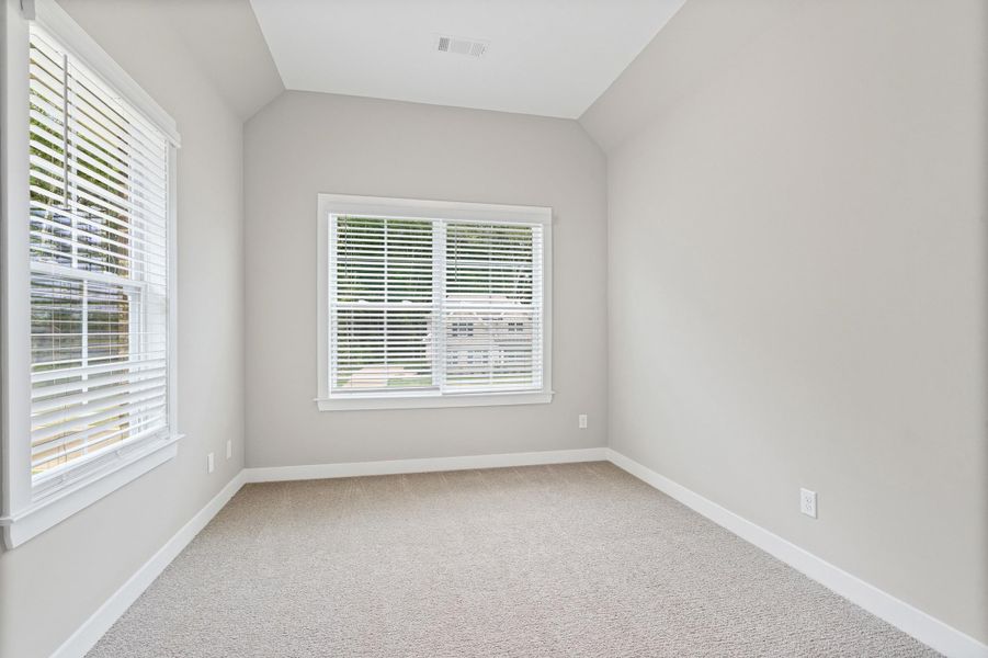 Neutral-toned carpet flooring and light gray walls define this room, featuring two windows with white blinds Neutral-toned carpet flooring and light gray walls define this room, featuring two windows with white blinds