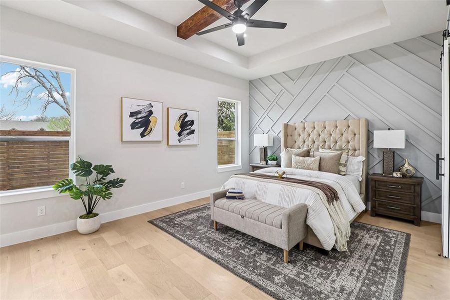 Bedroom with light wood-style floors, a ceiling fan, a tray ceiling, and an accent wall