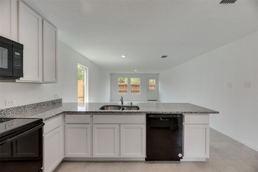 Kitchen with sink, black appliances, kitchen peninsula, and light stone countertops