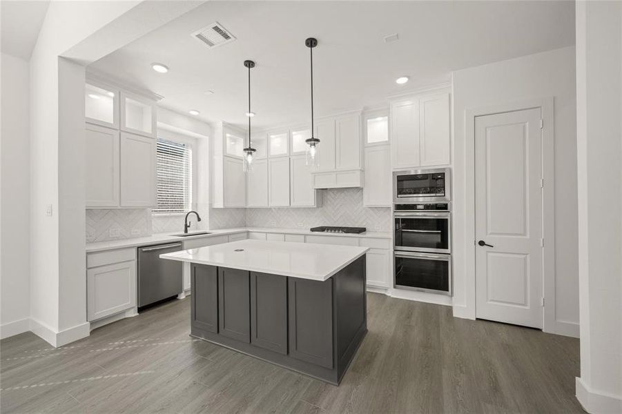 Two tone kitchen with stainless steel appliances, glass insert cabinets, two tone cabinetry, tasteful backsplash, and hanging light fixtures