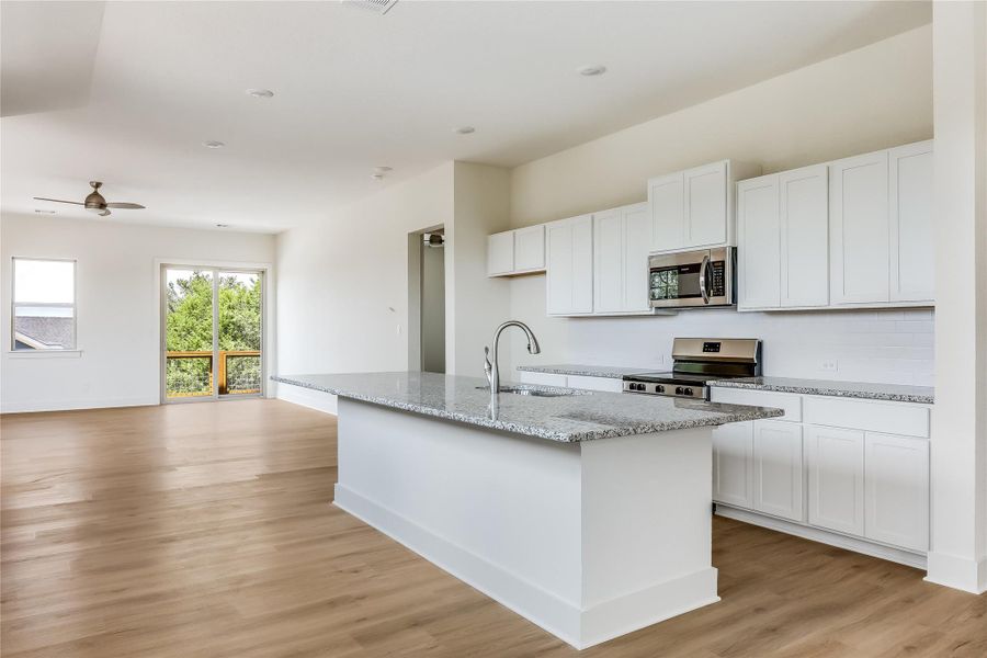 Kitchen with white cabinetry, stainless steel appliances, a kitchen island with sink, and light wood finished floors