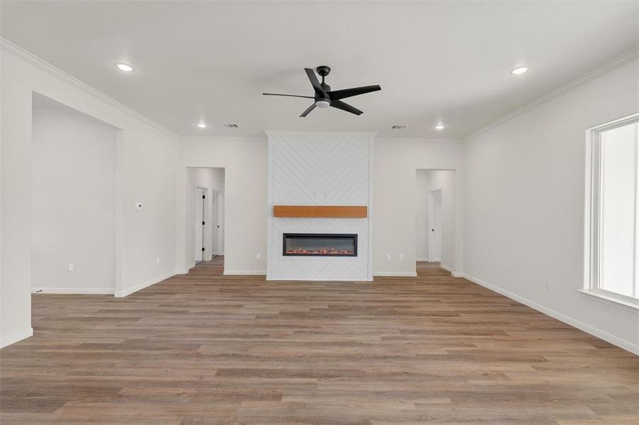 Unfurnished living room with ceiling fan, light wood-style floors, ornamental molding, a large fireplace, and recessed lighting Unfurnished living room with ceiling fan, light wood-style floors, ornamental molding, a large fireplace, and recessed lighting