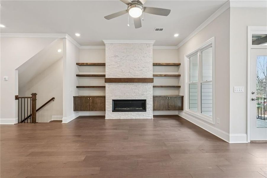 Unfurnished living room with dark wood-style flooring, a ceiling fan, crown molding, a fireplace, and recessed lighting