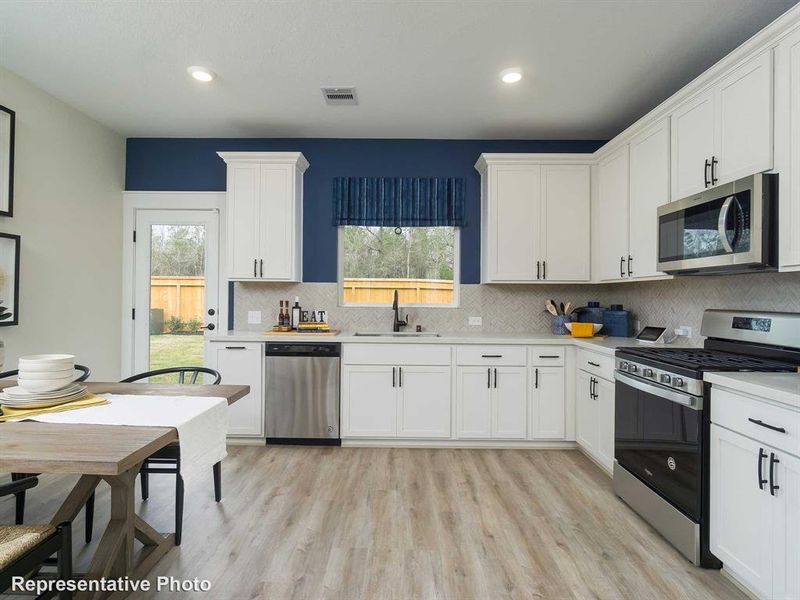 Kitchen featuring stainless steel appliances, decorative backsplash, white cabinetry, light wood-style floors, and recessed lighting