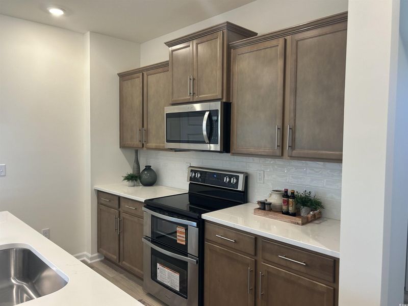 Kitchen featuring appliances with stainless steel finishes, backsplash, light stone countertops, and light wood-style floors