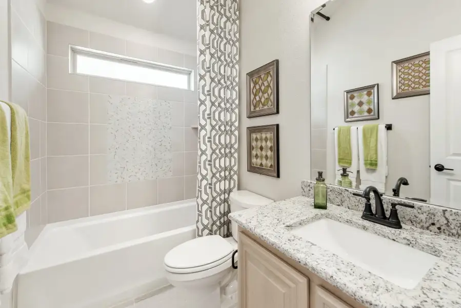Full bathroom with granite countertop vanity, tiled tub-shower combo, and patterned curtain