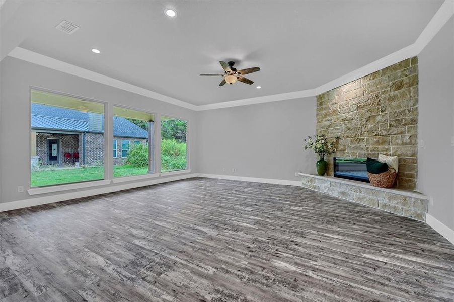 Unfurnished living room with a fireplace, ornamental molding, dark wood-type flooring, and ceiling fan