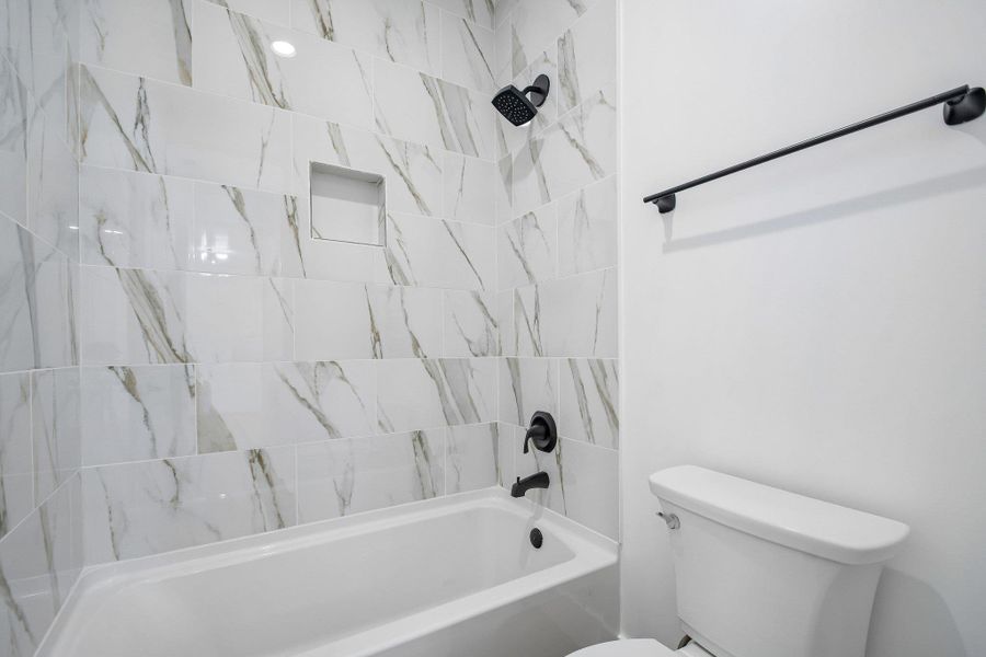 Polished tile walls surround a deep soaking tub featuring matte black hardware. Polished tile walls surround a deep soaking tub featuring matte black hardware.