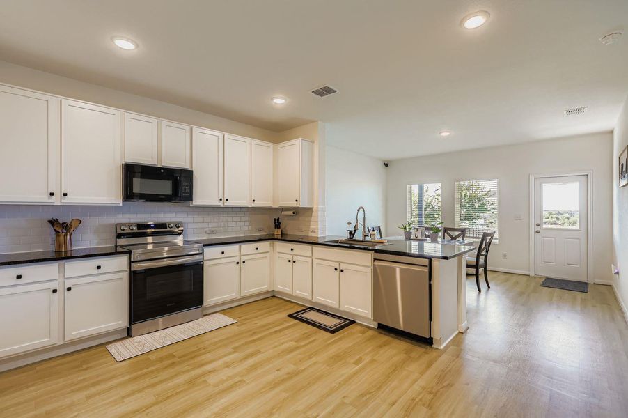 Kitchen with stainless steel appliances, backsplash, white cabinets, a peninsula, and recessed lighting