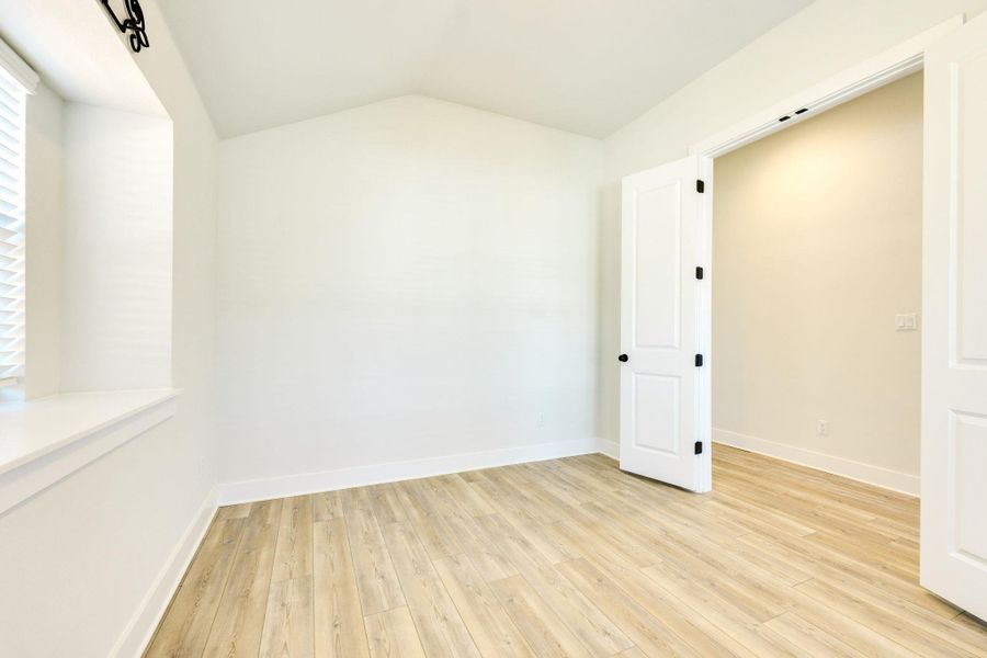 Empty room with lofted ceiling, light wood-style flooring, and healthy amount of natural light