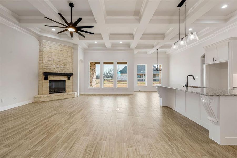 Unfurnished living room featuring a stone fireplace, ceiling fan, crown molding, beam ceiling, and sink