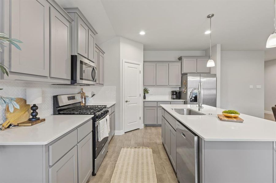Kitchen featuring light gray cabinetry, white countertops, stainless steel appliances, a gas range, and a central island with an undermount sink Kitchen featuring light gray cabinetry, white countertops, stainless steel appliances, a gas range, and a central island with an undermount sink