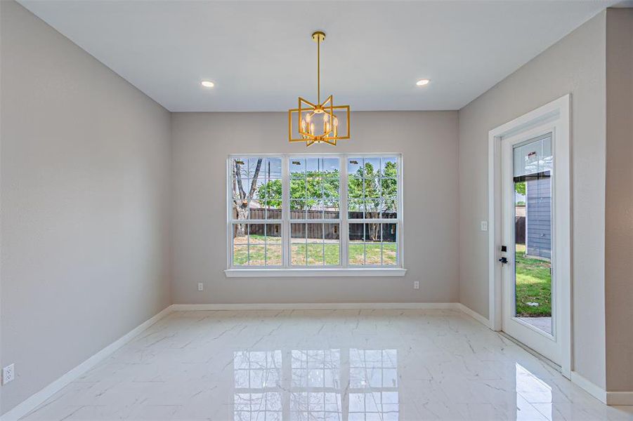 Unfurnished dining area featuring hanging lights, healthy amount of natural light, and light marble finish flooring