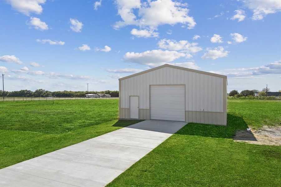 Steel-frame outbuilding featuring a roll-up door, pedestrian entry door, and concrete drive