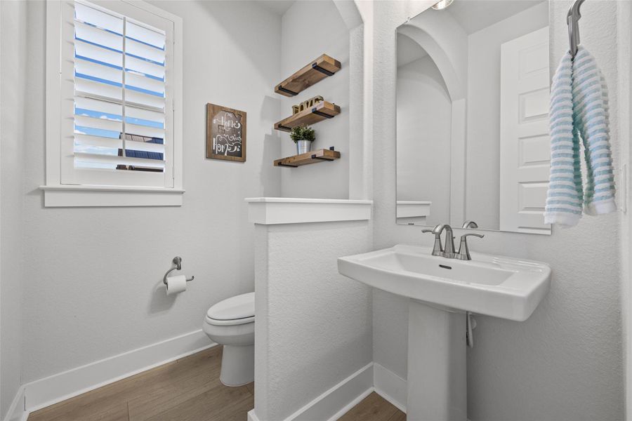 A well-appointed powder room features a pedestal sink and modern wood-look flooring.