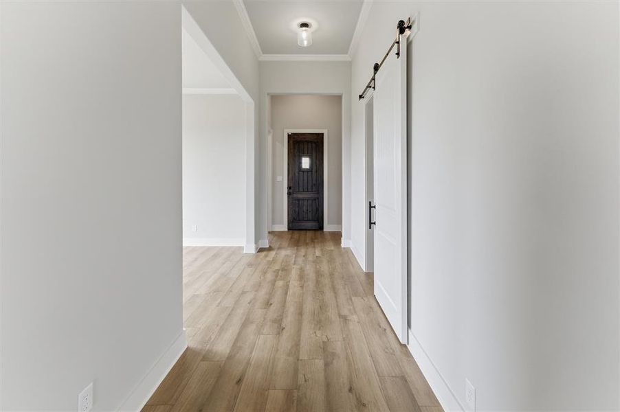 Corridor featuring a barn door, ornamental molding, and light wood finished floors
