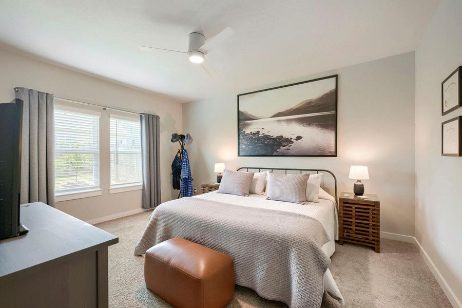 A comfortable bedroom with a ceiling fan, two large windows providing natural illumination, and soft carpet underfoot. A comfortable bedroom with a ceiling fan, two large windows providing natural illumination, and soft carpet underfoot.