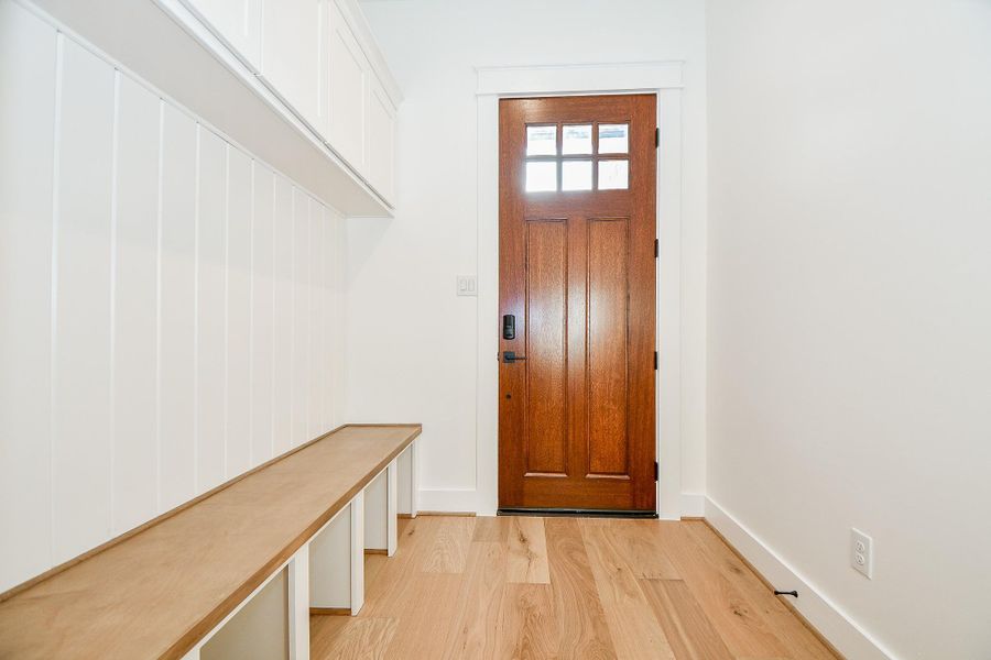 The mudroom provides a practical yet stylish drop zone. Featuring built-in cubbies, a long wood bench, upper cabinetry for hidden storage, and classic board-and-batten detailing, this space keeps daily clutter neatly tucked away. The warm wood door adds a rustic-modern charm, perfectly tying in with the rest of the home’s design. The mudroom provides a practical yet stylish drop zone. Featuring built-in cubbies, a long wood bench, upper cabinetry for hidden storage, and classic board-and-batten detailing, this space keeps daily clutter neatly tucked away. The warm wood door adds a rustic-modern charm, perfectly tying in with the rest of the home’s design.