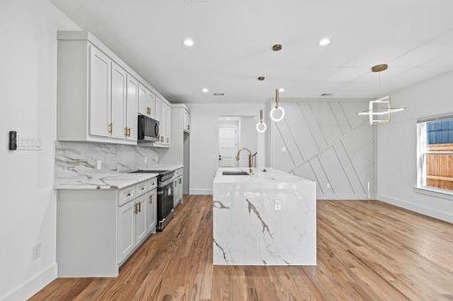 Kitchen with white cabinetry, pendant lighting, stainless steel appliances, and light stone counters