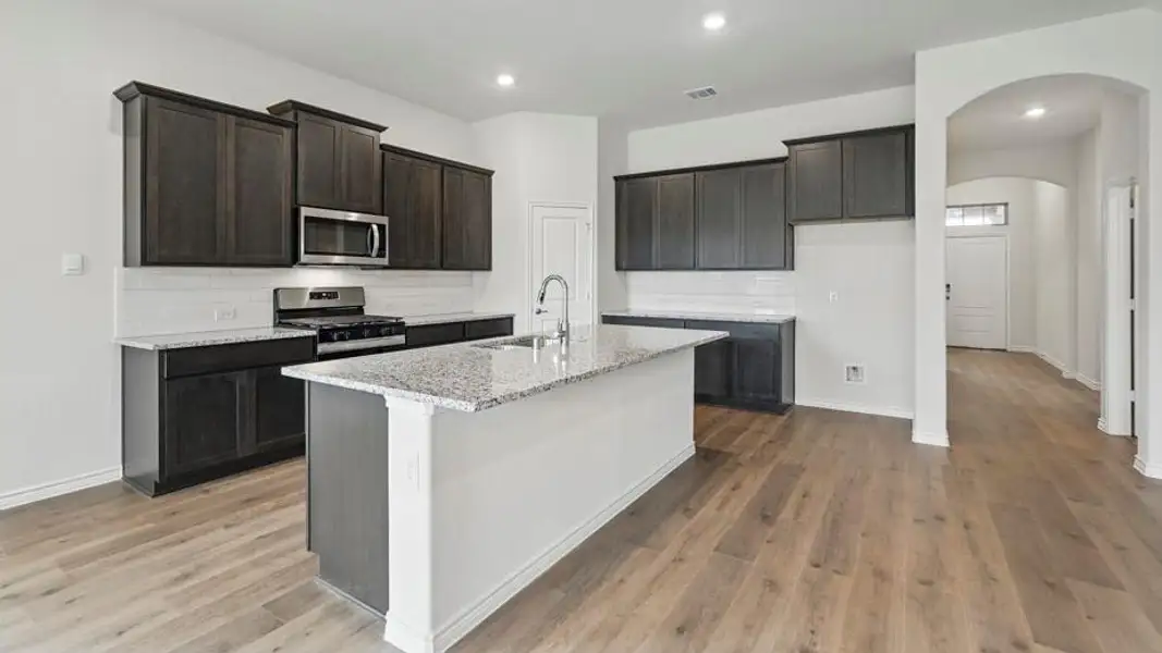 Kitchen featuring a central island with a sink, stainless steel appliances, dark wood cabinetry, and light-toned countertops