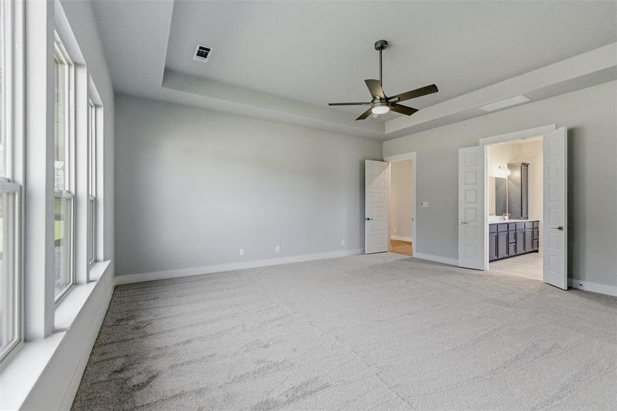 Unfurnished bedroom with a tray ceiling, light carpet, a ceiling fan, and ensuite bathroom