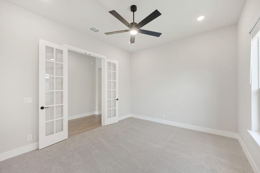 Empty bedroom with gray carpet, black ceiling fan, and white French doors leading to closet