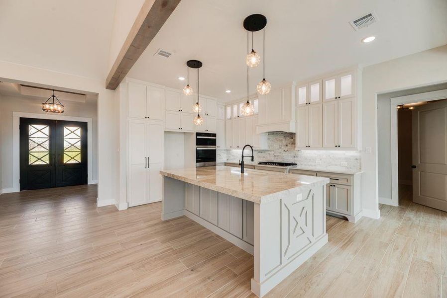 Kitchen with light wood-style floors, light stone counters, a center island with sink, white cabinetry, and beam ceiling