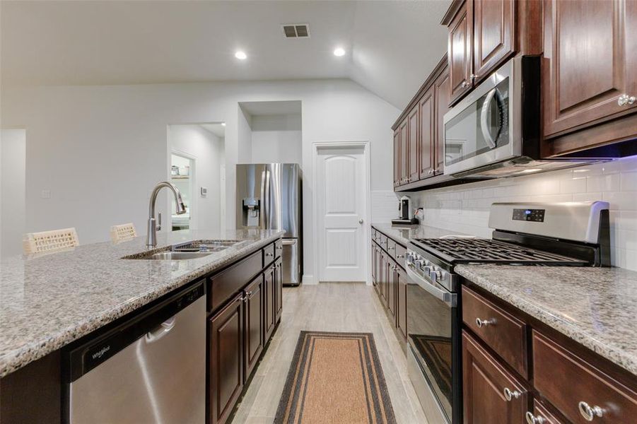 Kitchen with backsplash, sink, light hardwood / wood-style floors, light stone counters, and stainless steel appliances