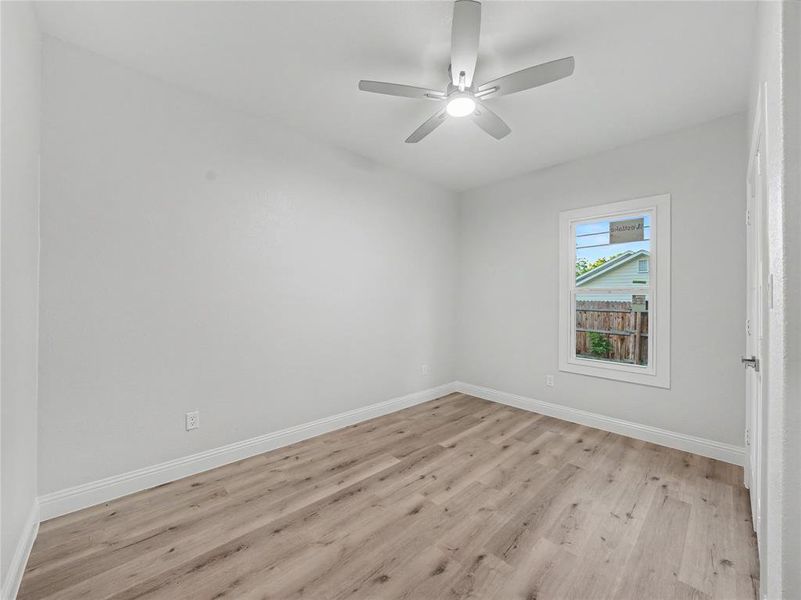 Room with wood-finish flooring, a white ceiling fan with integrated lighting, and a white-framed window