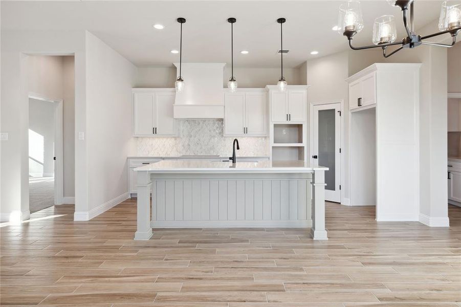 Kitchen with pendant lighting, white cabinets, decorative backsplash, an island with sink, and a notable chandelier