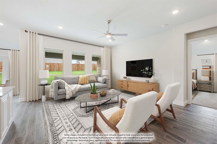 Open living room with gray sofa, ceiling fan, wood-look floors, and large windows overlooking backyard