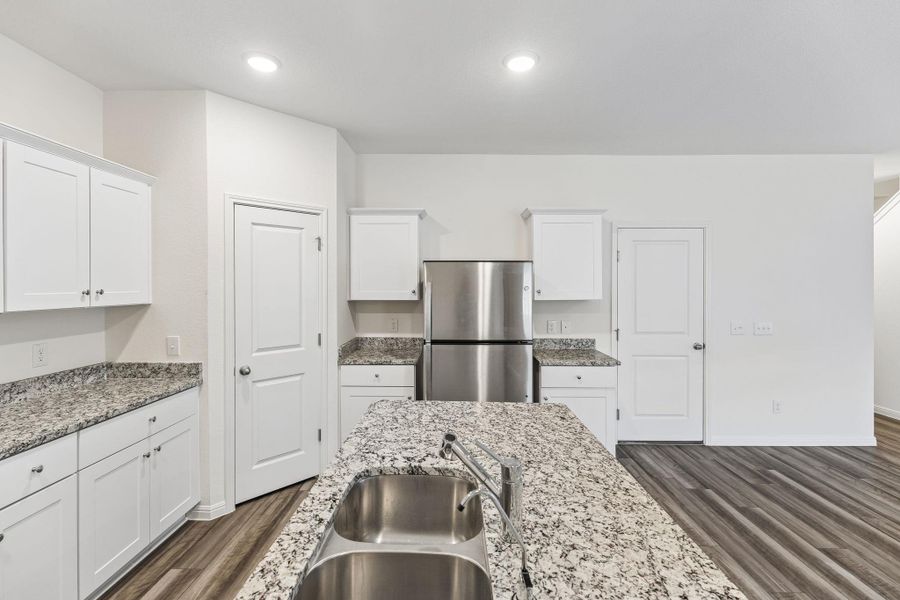 Kitchen with white cabinetry, freestanding refrigerator, dark wood-type flooring, light stone counters, and recessed lighting