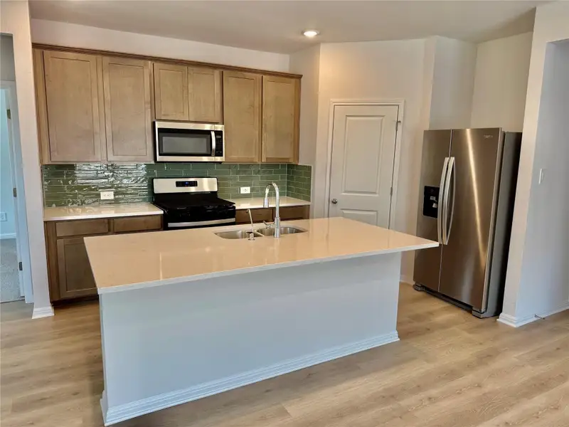 Kitchen with appliances with stainless steel finishes, decorative backsplash, light stone counters, and a center island with sink