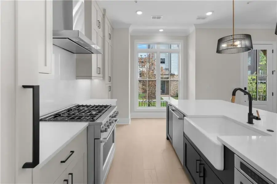 Gourmet kitchen featuring a gas range with stainless steel hood, white shaker cabinetry, light wood-finish flooring, a kitchen island with a farmhouse sink, and a modern chandelier