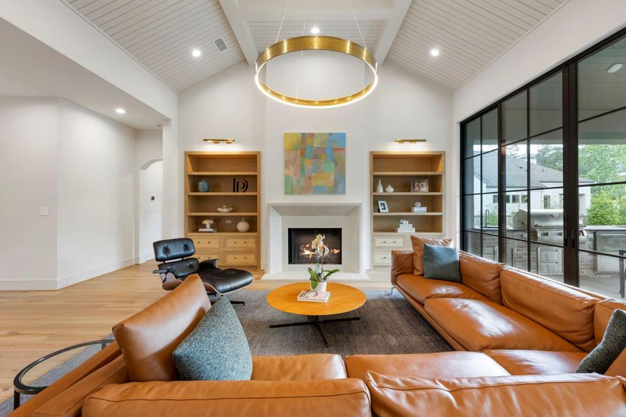 Stunning living room with vaulted ceilings, a statement chandelier, built-in shelving, and a sleek fireplace, all complemented by expansive glass doors that open to the outdoor living area for seamless indoor-outdoor entertaining.
