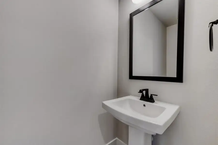 Pedestal sink featuring a matte black faucet and a framed mirror
