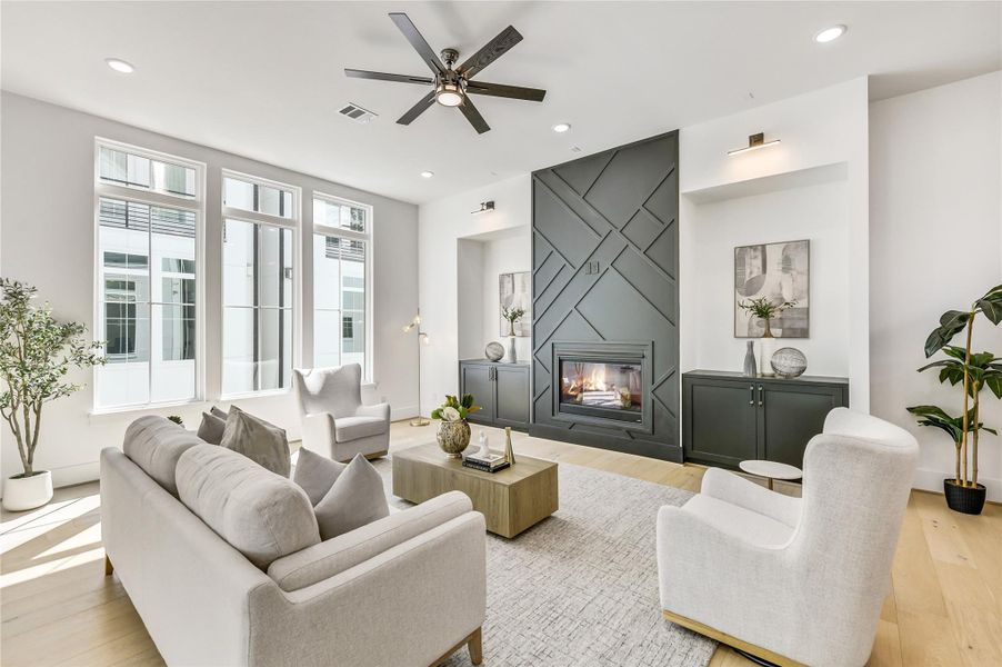 Expansive living room flooded with natural light through energy-efficient floor-to-ceiling windows. The focal wall features custom geometric millwork surrounding a sleek gas fireplace with built-in cabinetry—an elevated blend of form and function. Designer lighting, high ceilings, and wide-plank European white oak floors complete the sophisticated aesthetic. Expansive living room flooded with natural light through energy-efficient floor-to-ceiling windows. The focal wall features custom geometric millwork surrounding a sleek gas fireplace with built-in cabinetry—an elevated blend of form and function. Designer lighting, high ceilings, and wide-plank European white oak floors complete the sophisticated aesthetic.