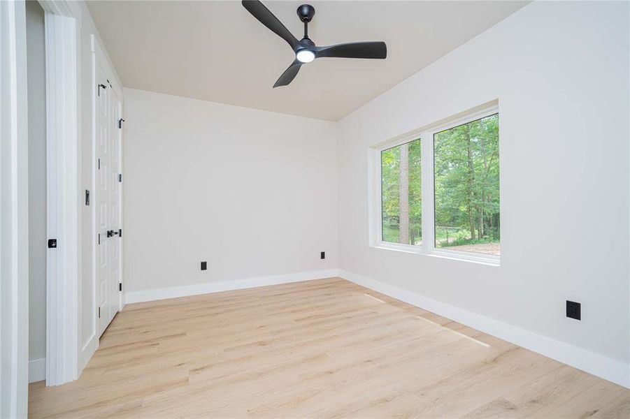Spacious room featuring wood-finish flooring, white walls, and a black ceiling fan