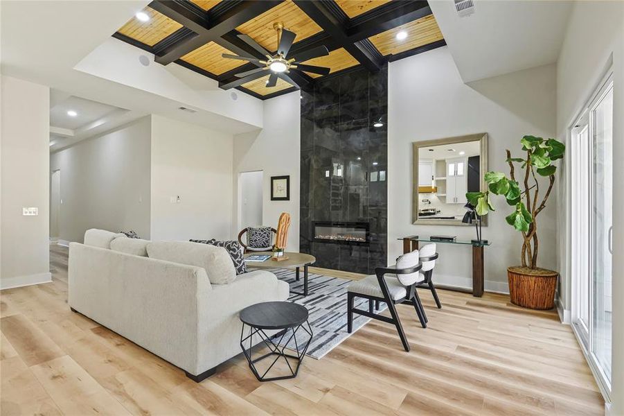 Living area with coffered ceiling, light wood finished floors, a high wood beamed ceiling, a tile fireplace, and a ceiling fan