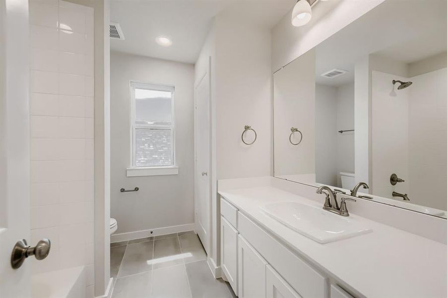 Bathroom featuring a white vanity with an integrated sink, a large mirror, a shower with white subway tile, and light gray floor tiles