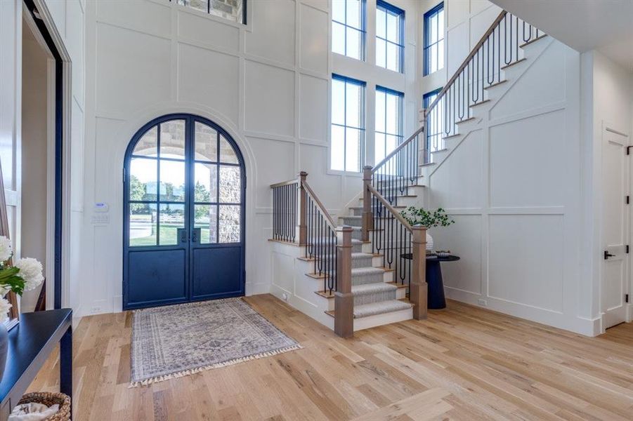 Entryway featuring a decorative wall, stairway, healthy amount of natural light, wood finished floors, and a high ceiling Entryway featuring a decorative wall, stairway, healthy amount of natural light, wood finished floors, and a high ceiling